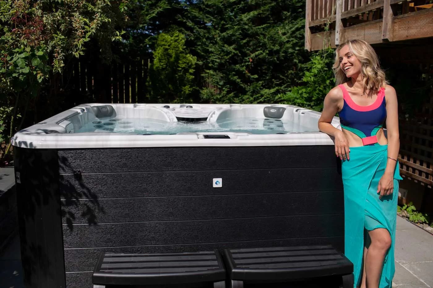Woman standing beside a Clearwater Spas hot tub with a dark cabinet and matching steps on a backyard patio