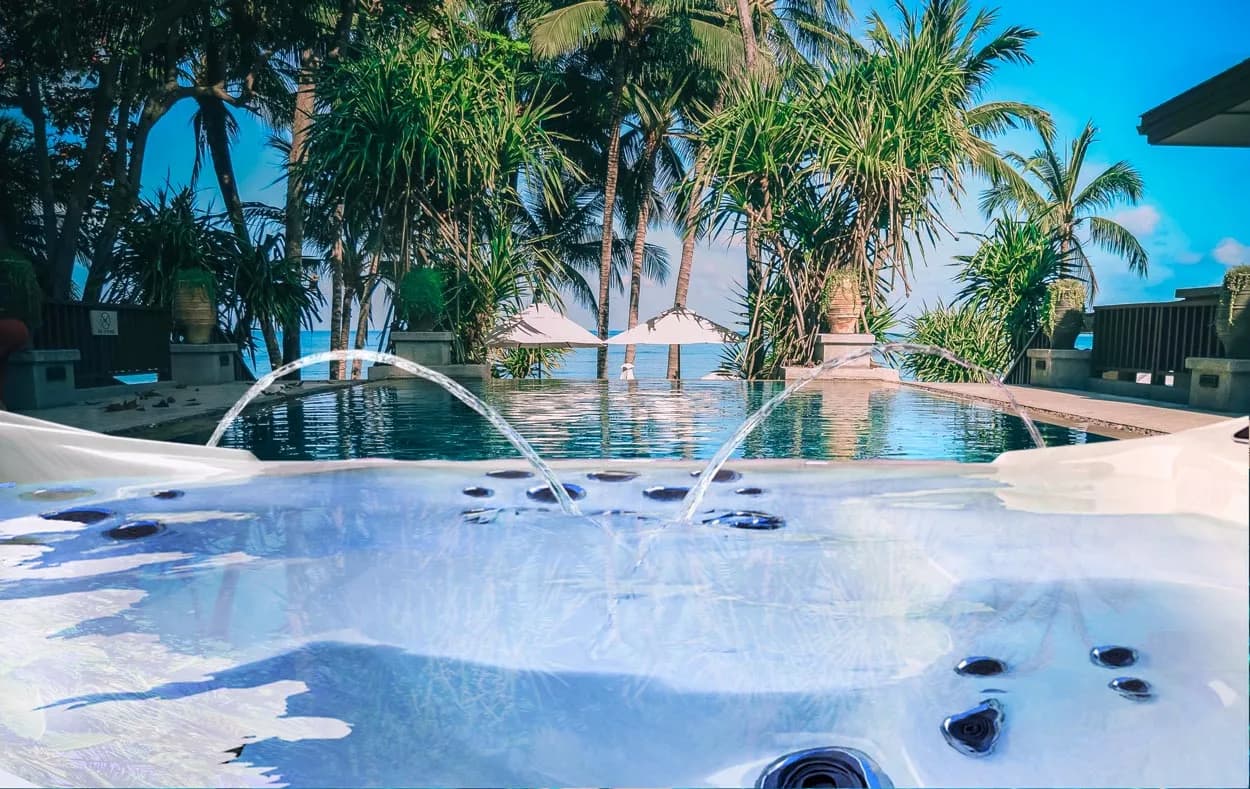 Coast Spas Infinity Edge hot tub with water fountains, looking out over a pool and palm trees