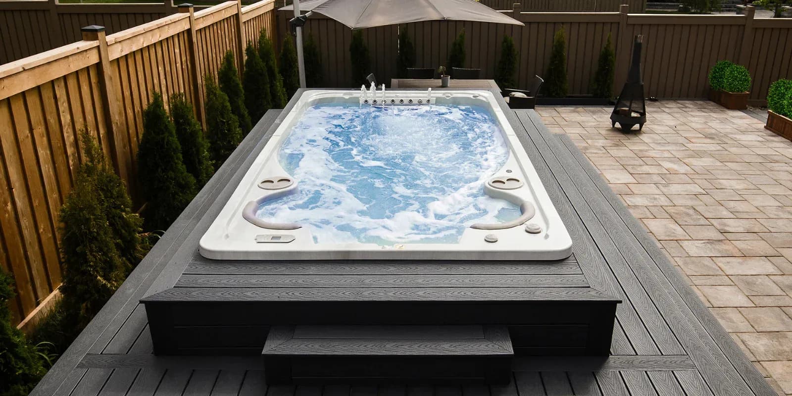 Hydropool swim spa with its jets running, set into a raised composite deck with steps in a fenced backyard