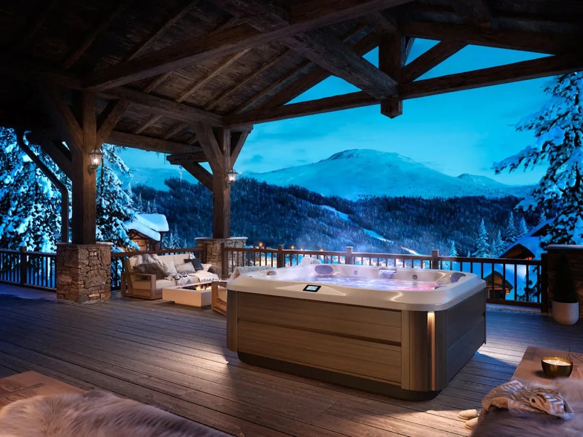 Jacuzzi J-385 hot tub installed on a covered chalet deck at dusk with snowy mountains behind