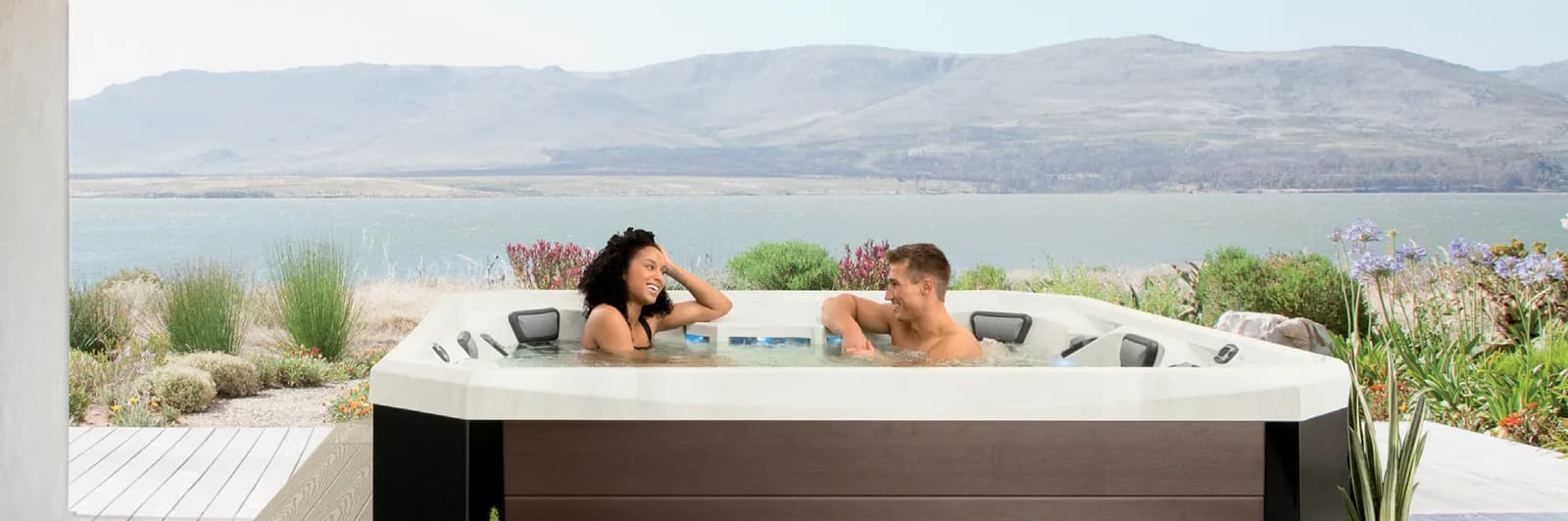 Couple in a Marquis Vector21 V94 hot tub overlooking a lake and mountains
