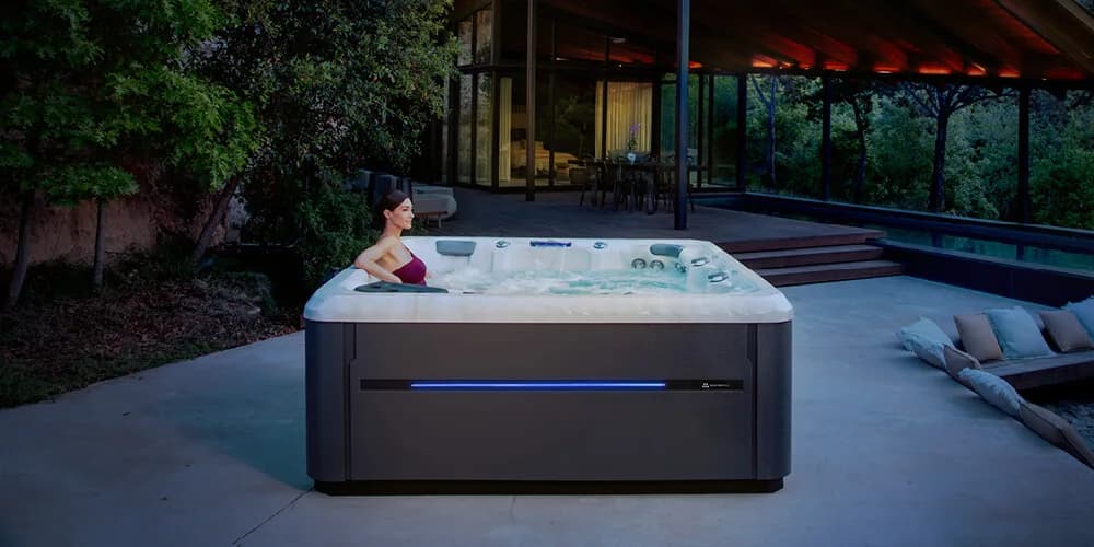 Master Spas Twilight TS 8.2 hot tub installed on a patio at dusk with cabinet lighting on