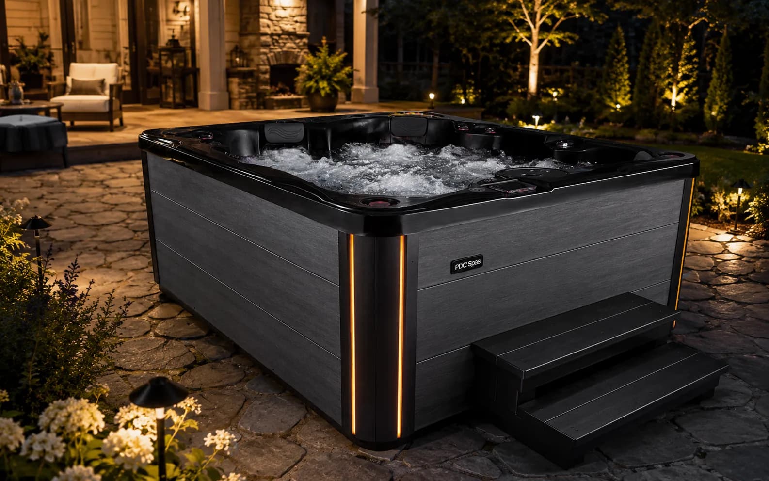 PDC Spas Midnight Series Biscayne hot tub with corner lighting on a stone patio at night
