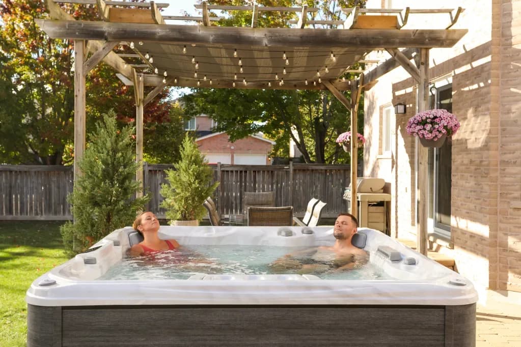 Couple relaxing in a Sundance Chelsee 780 hot tub under a pergola